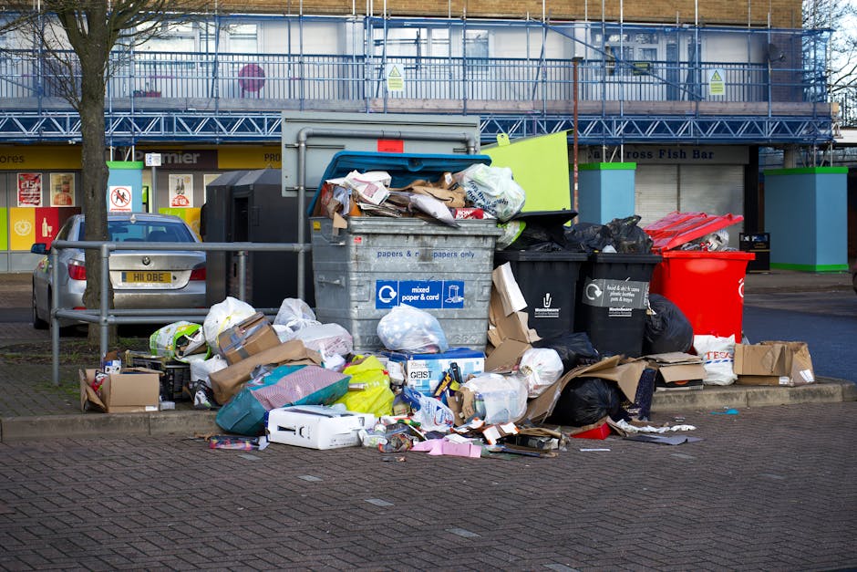 A person is seen discarding brown paper bags into a white rubbish bin, which has a flip-top lid that is partly open. The paper bags vary in size and texture, with some appearing crumpled and others re